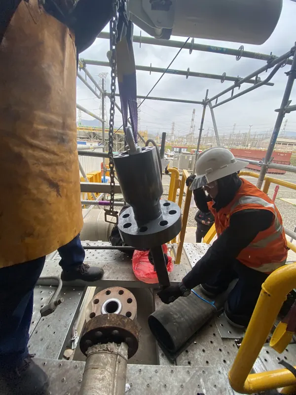 Técnicos montan una válvula izada con tecle sobre una plataforma en planta